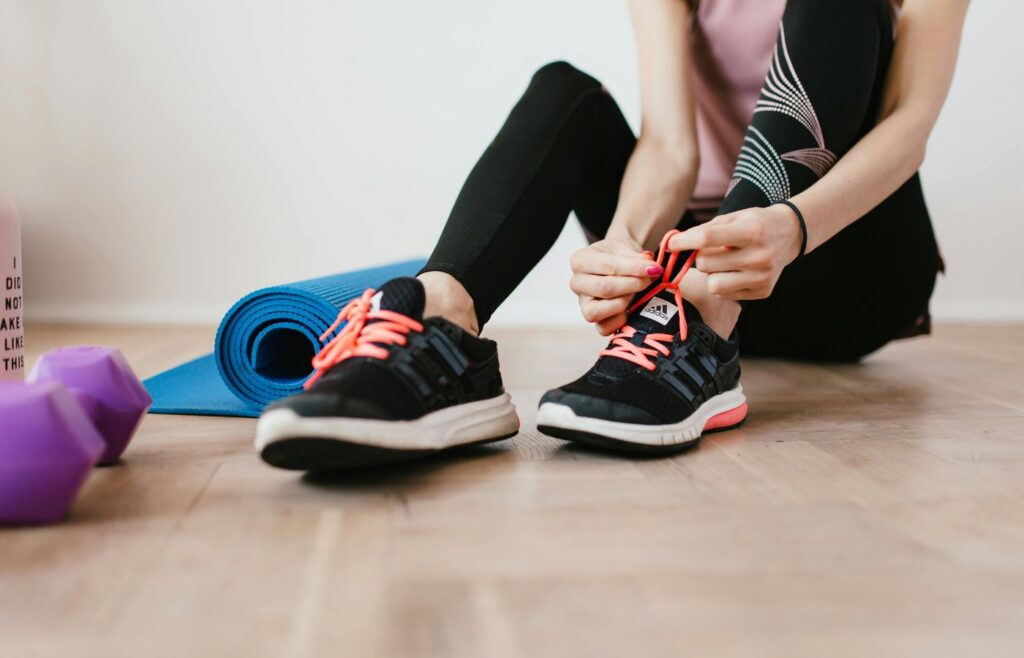 Anonymous slender female athlete tying shoelaces near sport accessories