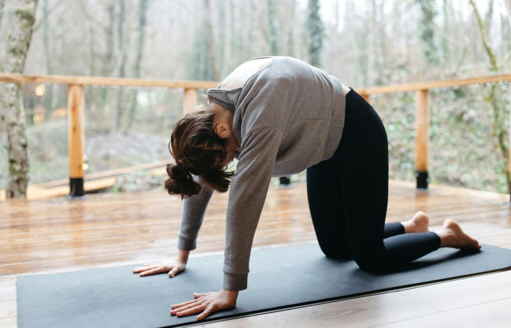 Woman in Gray Long Sleeve Shirt and Black Leggings Doing Yoga on Black Yoga Mat