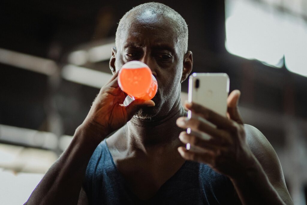 Man in Blue Tank Top Using Cellphone While Drinking